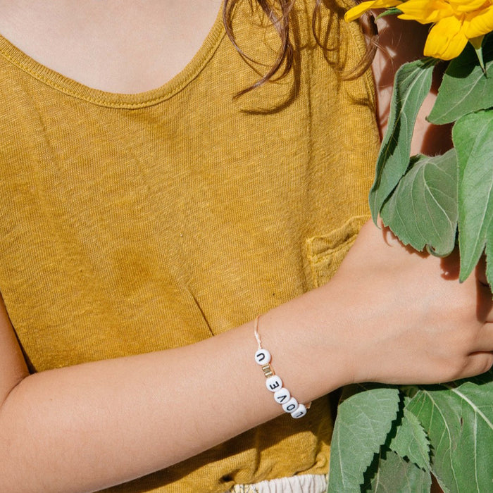 The LOVE U Charm Bracelet from French label Bbuble is a chic and cool cord bracelet for children composed of white letter beads, a gold heart on a cream color cord.